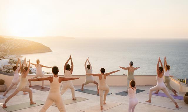 Clase de yoga al amanecer sobre una terraza mediterránea con vistas al mar
